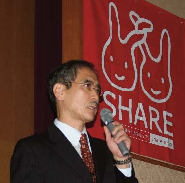 El Dr. Toru Honda abre el Seminario SHARE en Tokio titulado "Imaginando el futuro: ¿Es posible la salud para todos?". Arriba a su derecha está el logotipo SHARE.