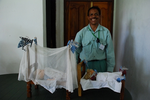 Julio, el PSF, muestra los modelos que hizo de mosquiteras y mosquitos, para mostrar cómo las redes protegen a un niño de la malaria.