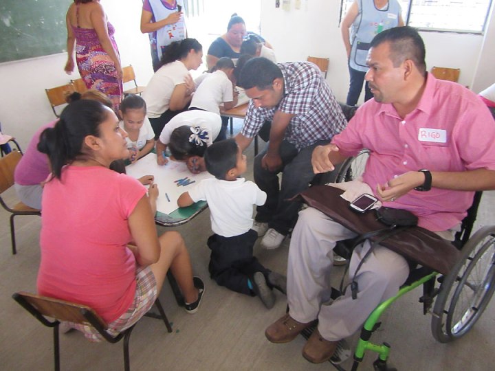 En un salón de clases en Los Pargos, Rigo, un psicólogo social, (en silla de ruedas) ayuda a los miembros de Habilítate a aprender el espíritu y la metodología de Niño-a-Niño, adaptándolo para mejorar la inclusión de niños discapacitados. Las madres y otros familiares de los niños también fueron invitados a participar.