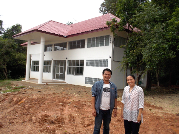 Cherry y Thom, líderes dedicados de Salud Compartida, se paran frente al nuevo centro del programa en el Hospital Khemarat. El edificio se construyó como un lugar de reunión para la capacitación de promotores de salud, reuniones LGTB, reuniones de personas con VIH-SIDA, actividades de aprendizaje de Amigos y Compañeros del Hogar y talleres comunitarios.