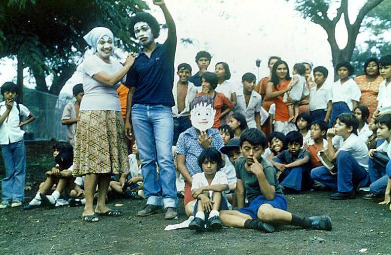 2. Al principio, para llamar la atención de la gente, los actores (un papá, una mamá y sus hijos) se paran como estatuas en medio de la calle. Papá tiene el puño cerrado en alto, simbolizando el triunfo de la revolución.