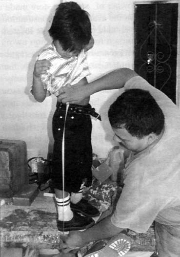 Armando, a disabled worker at PROJIMO, takes measurements to make twist cables for a boy with cerebral palsy, whose feet turn inward.