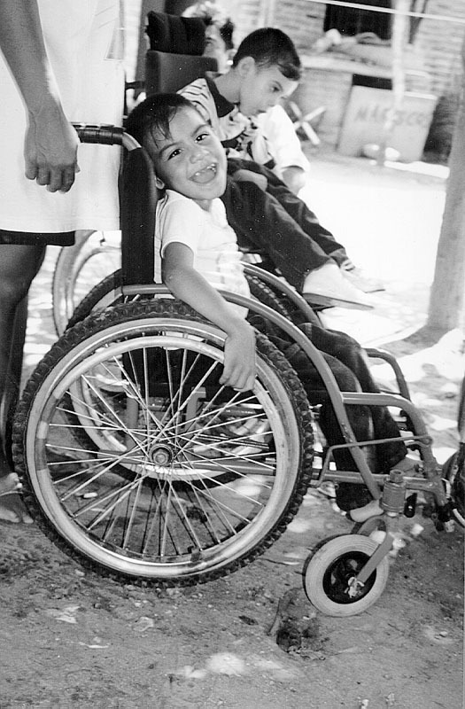 A young boy who has cerebral palsy tries out a new wheelchair which the PROJIMO Skills Training and Work Program has made for him. These chairs are carefully built and adapted to the size and needs of the individual child.