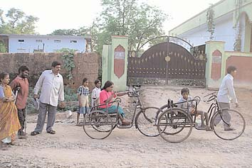 Children ride their trikes to school on rough roads.