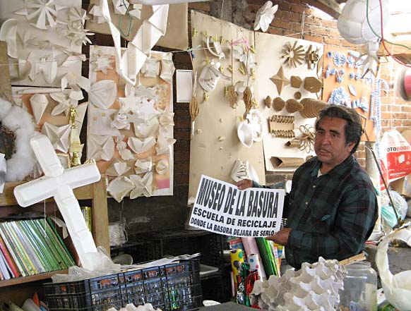 "GARBAGE MUSEUM: SCHOOL OF RECYCLING— HERE TRASH STOPS BEING SO" says the sign held by Jose Herrera in his workshop. The walls of the shop are covered with crafts and decorative "plastic arts" made from such things as paper plates, plastic cups, and cardboard egg-boxes.