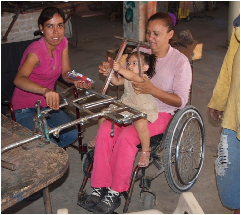 Not to be left out, Yasmín's 3-year-old daughter, sitting in Carmin's lap, does her best to help sand the frames.